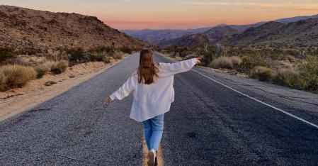 Una au pair corre por la autopista en el desierto con los brazos extendidos