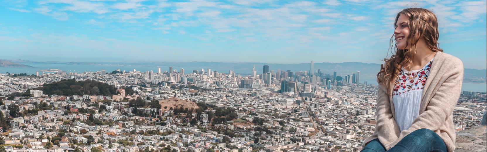 Una au pair sentada en un muro contemplando una ciudad.